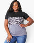 A woman modeling a short-sleeve color-block top with a black upper section, a gray and black leopard print middle band, and a muted purple-gray lower section, paired with blue jeans against a light gray studio background.