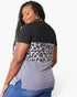 A woman wearing a short-sleeve color-block top with a black upper section, a gray leopard-print middle band, and a heather gray lower section, paired with blue jeans against a light gray background.