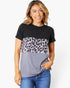 A woman wearing a short-sleeve colorblock t-shirt with a black top half, a gray leopard-print middle band, and a solid gray bottom half, paired with blue jeans against a white studio background.