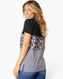 A woman wearing a short-sleeve colorblock top with a black upper section, a gray leopard-print middle panel, and a solid gray lower section, paired with blue jeans against a light gray studio background.