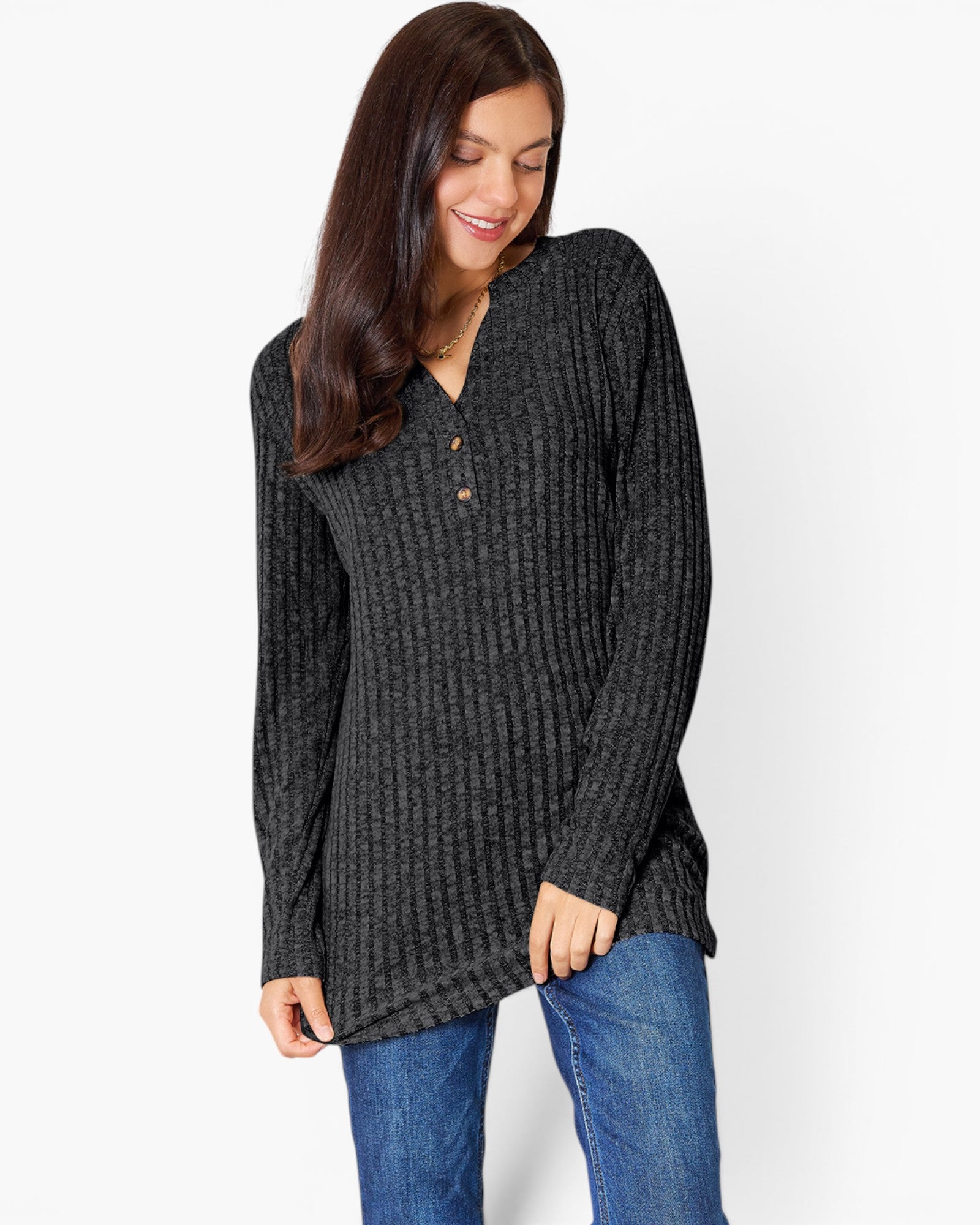 A woman wearing a dark charcoal gray ribbed knit tunic sweater with a buttoned split neckline, paired with blue jeans, against a plain white studio background.
