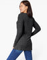 A woman wearing a dark charcoal gray ribbed knit long-sleeve top and blue jeans, photographed from a three-quarters back angle against a plain white studio background.