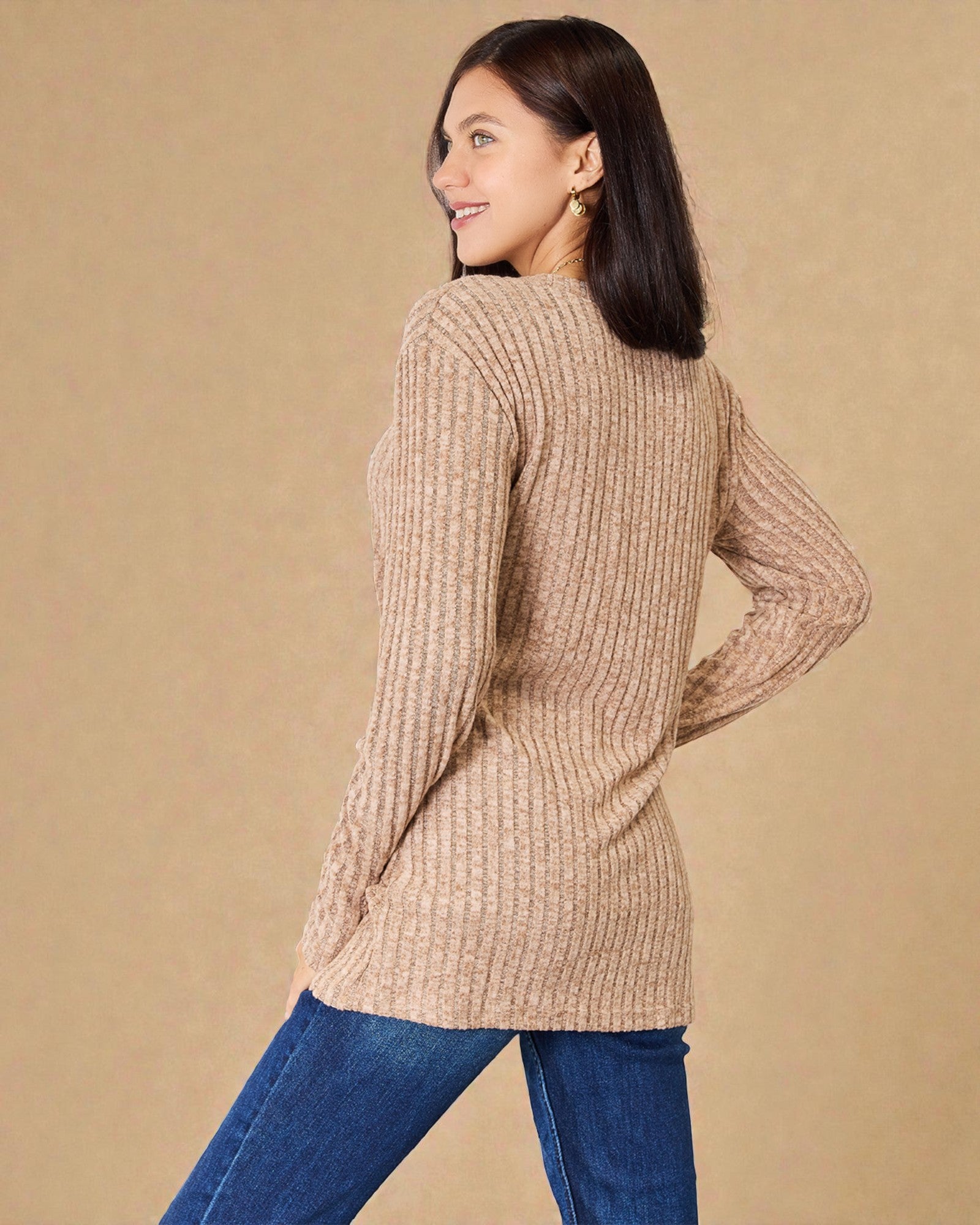 Woman wearing a beige sweater and blue jeans against a beige background