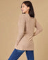 Woman wearing a beige sweater and blue jeans against a beige background