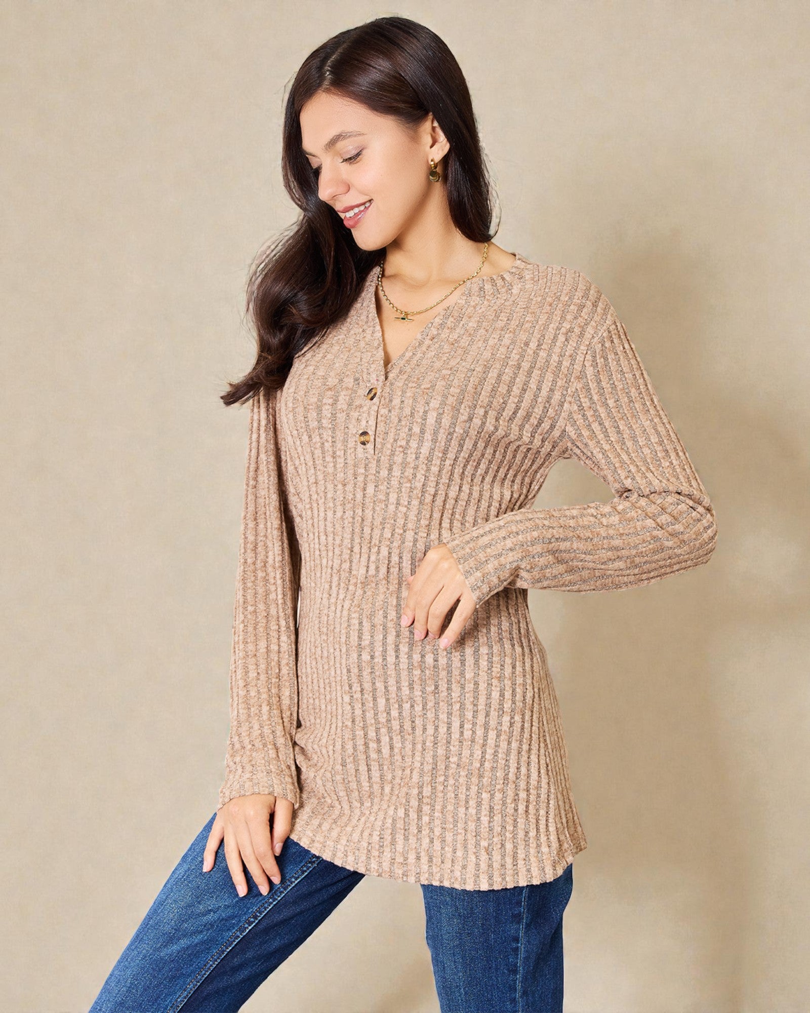 Woman wearing a beige long-sleeve knit top with a plain background
