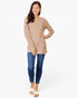 A woman modeling a beige ribbed knit long-sleeve henley tunic top with blue jeans and white slide sandals, standing against a plain white studio background.