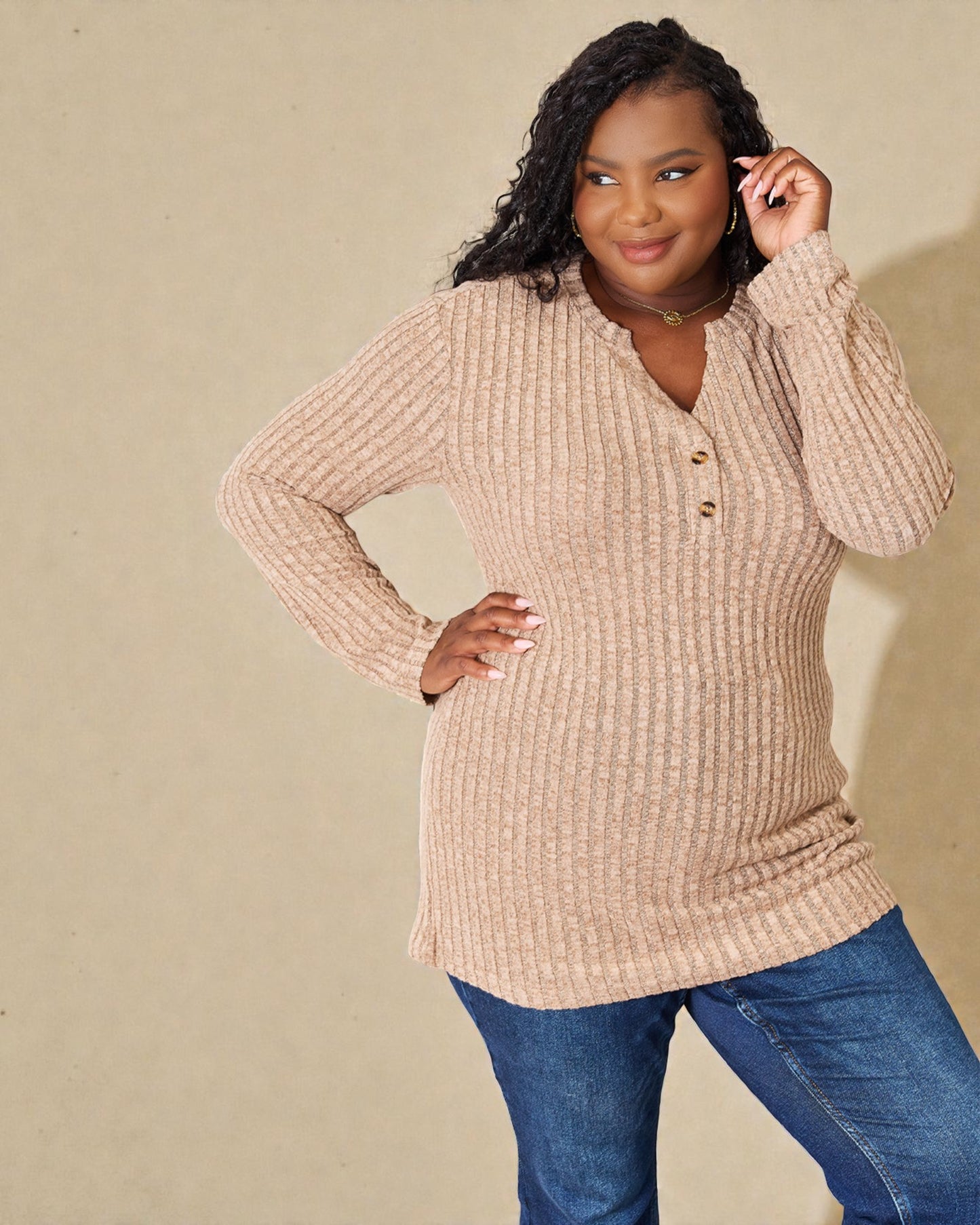 Woman wearing a beige ribbed sweater and blue jeans against a beige background