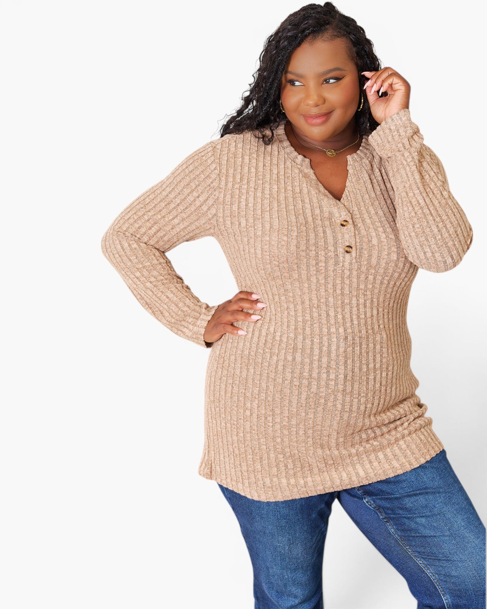 A woman modeling a beige ribbed knit long-sleeve henley top with blue jeans against a plain white studio background.