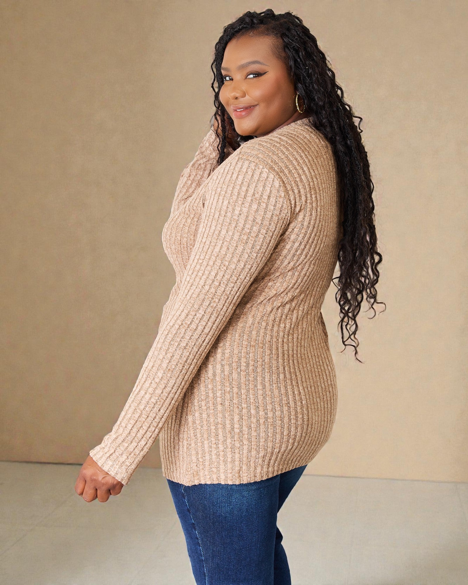 Woman wearing a beige ribbed sweater and blue jeans against a beige background