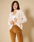 Woman wearing a beige cardigan and brown pants against a beige background