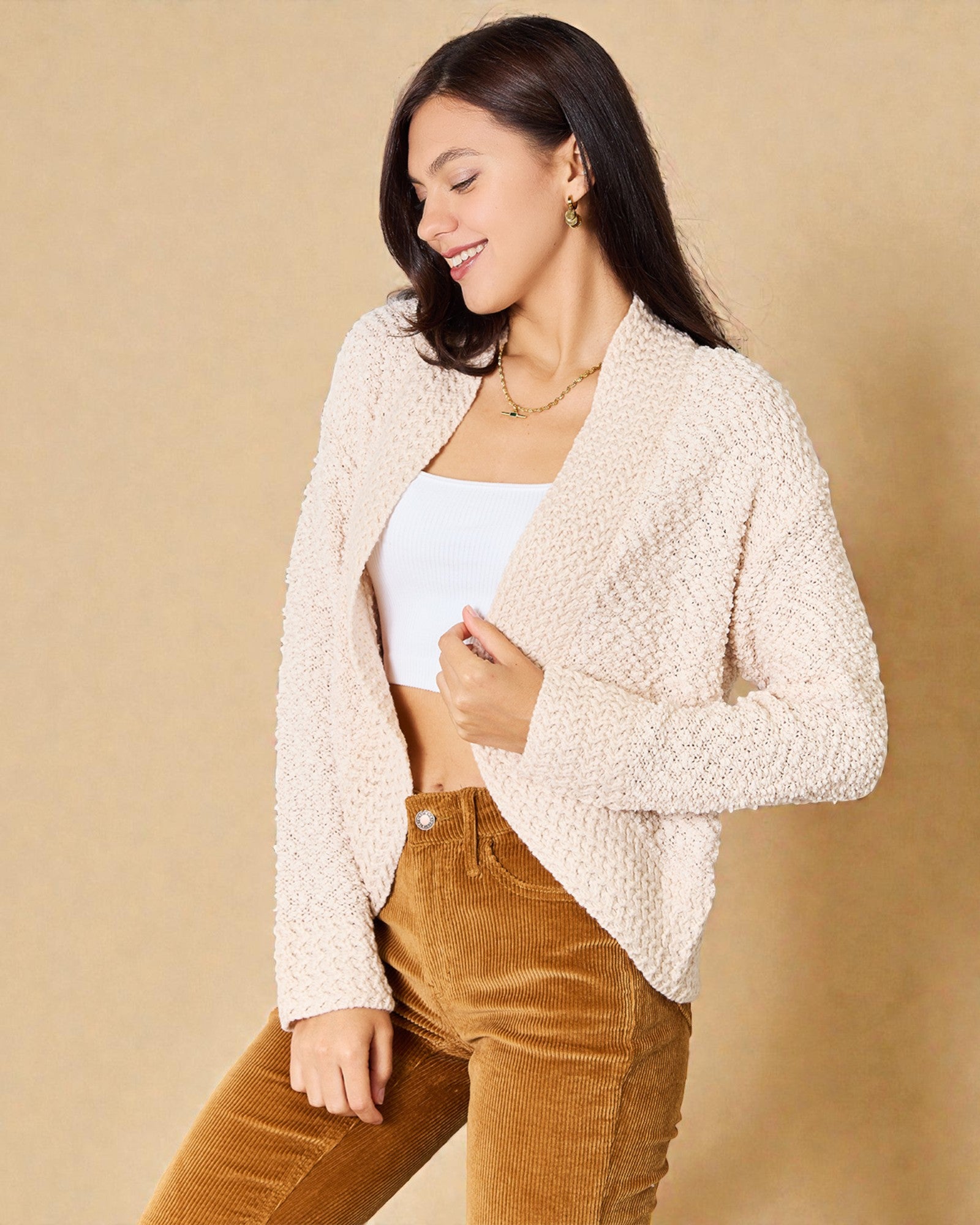 Woman wearing a beige cardigan over a white top and brown pants on a beige background