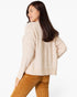 A woman wearing a textured cream-colored knit sweater and brown corduroy pants, shown from a side-back angle against a plain white studio background.