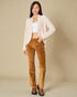 Woman wearing a beige cardigan, white top, and brown pants against a beige background
