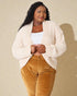 Woman wearing a cream cardigan and brown pants against a beige background