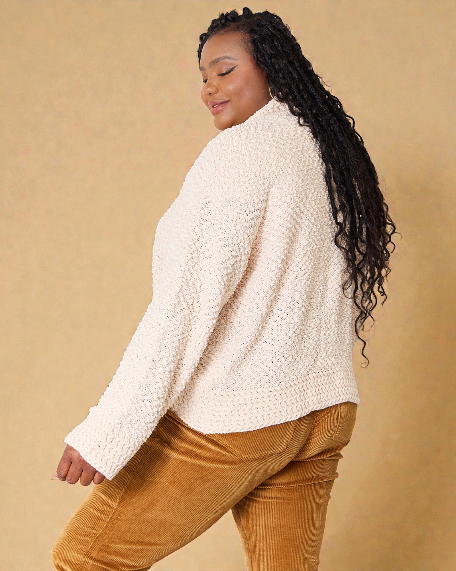 Woman wearing a cream sherpa sweater and brown pants against a beige background