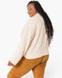 A woman wearing a cream-colored textured knit sweater and mustard brown corduroy pants, shown from a side-back angle against a plain white background.