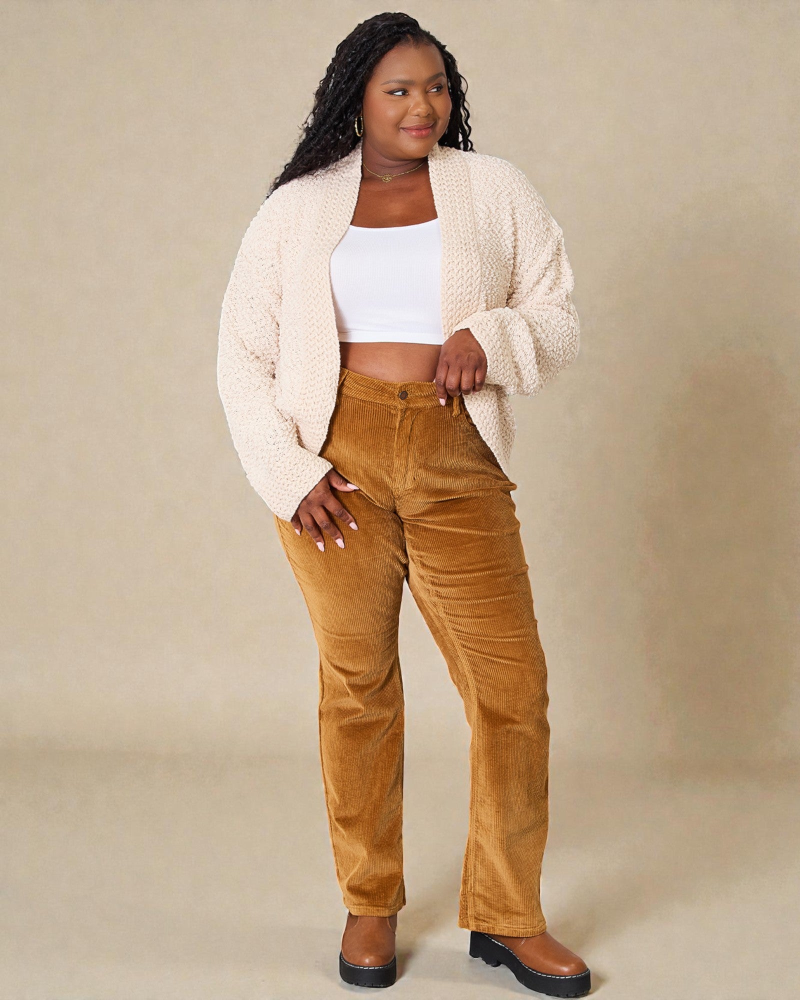 Woman wearing a cream cardigan, white top, and brown pants against a beige background