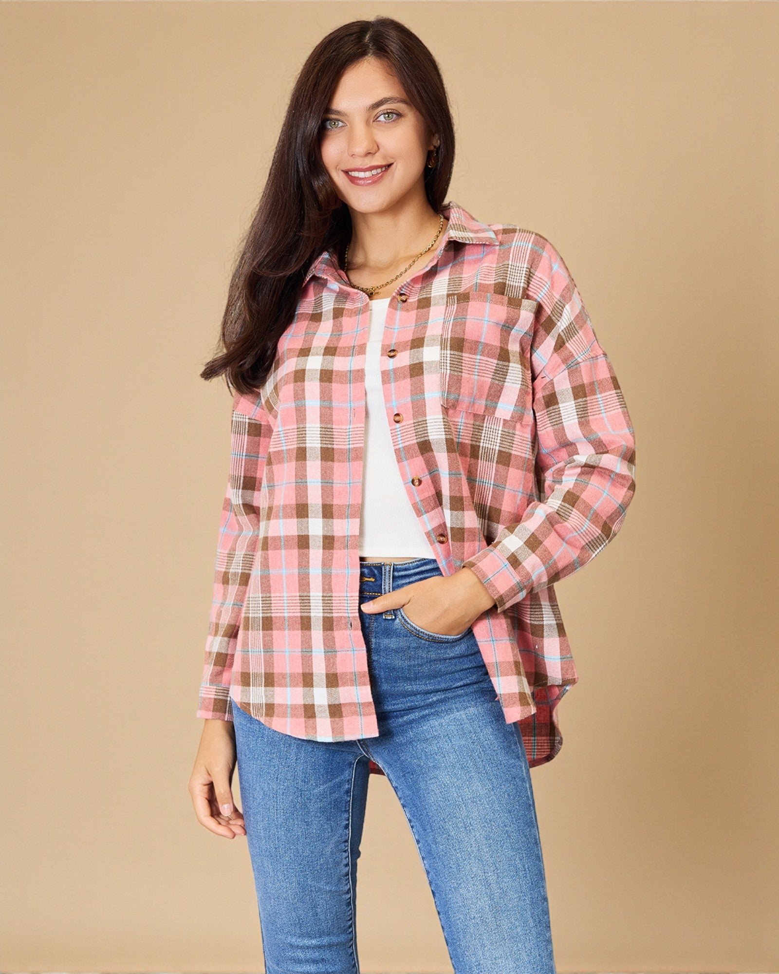 Woman wearing a pink and brown plaid shirt with blue jeans on a beige background