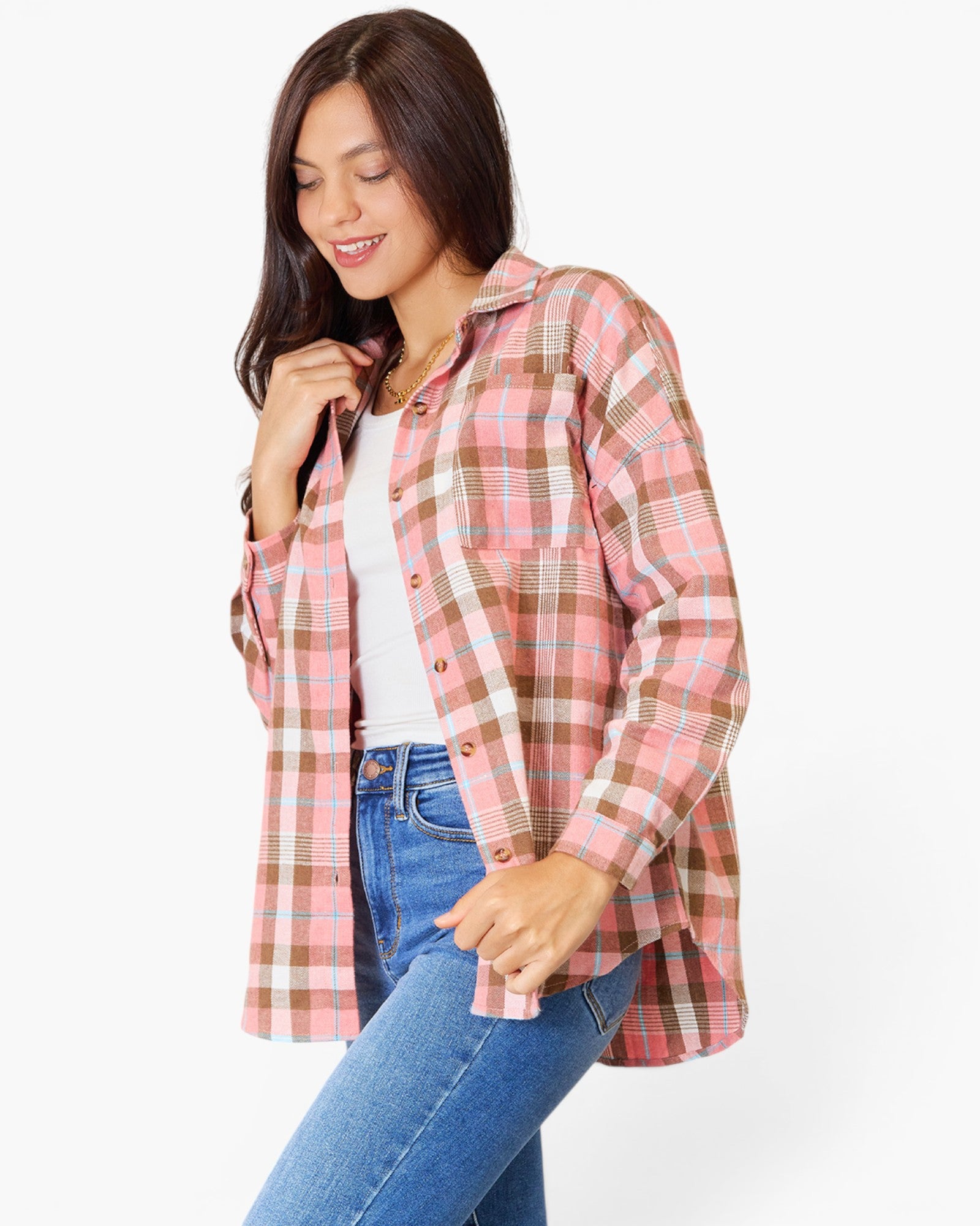 A woman wearing a pink, white, and brown plaid button-up shirt over a white top and blue jeans, posing against a light gray studio background.