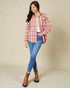 Woman wearing a pink plaid shirt, blue jeans, and brown boots on a beige background