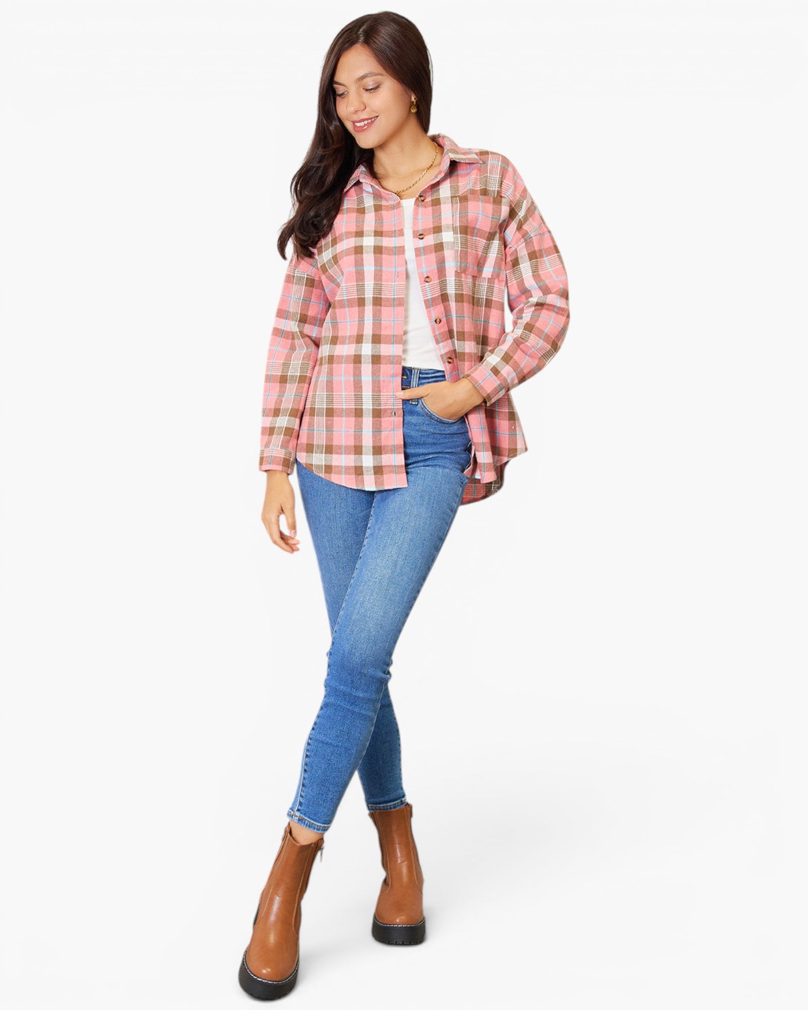 A woman modeling a pink and beige plaid button-up shirt over a white top, paired with blue skinny jeans and brown ankle boots, against a plain white background.