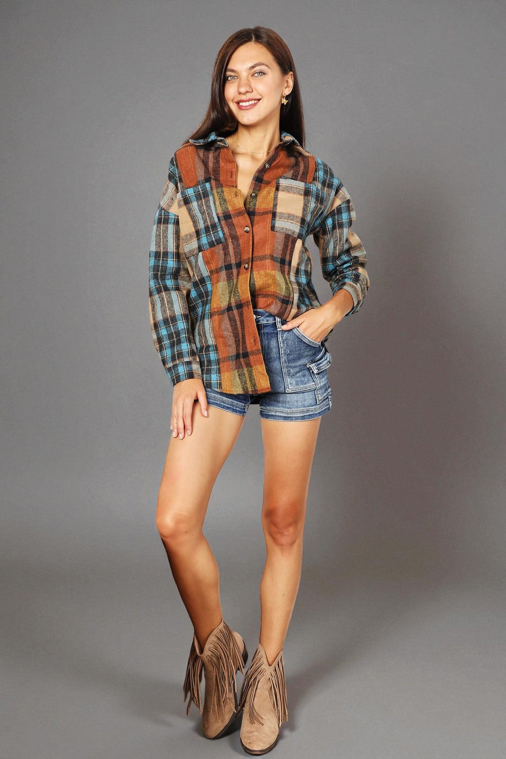 Woman wearing a plaid shirt, denim shorts, and fringed boots on a gray background