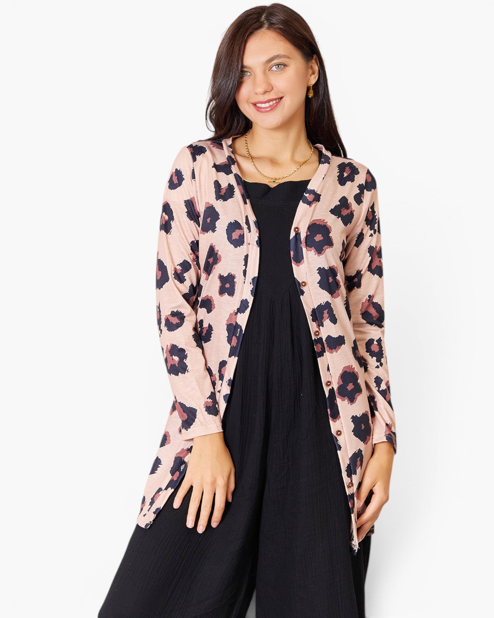 A woman modeling a light pink long-sleeve cardigan with a dark floral print, worn open over a black dress, against a plain white studio background.