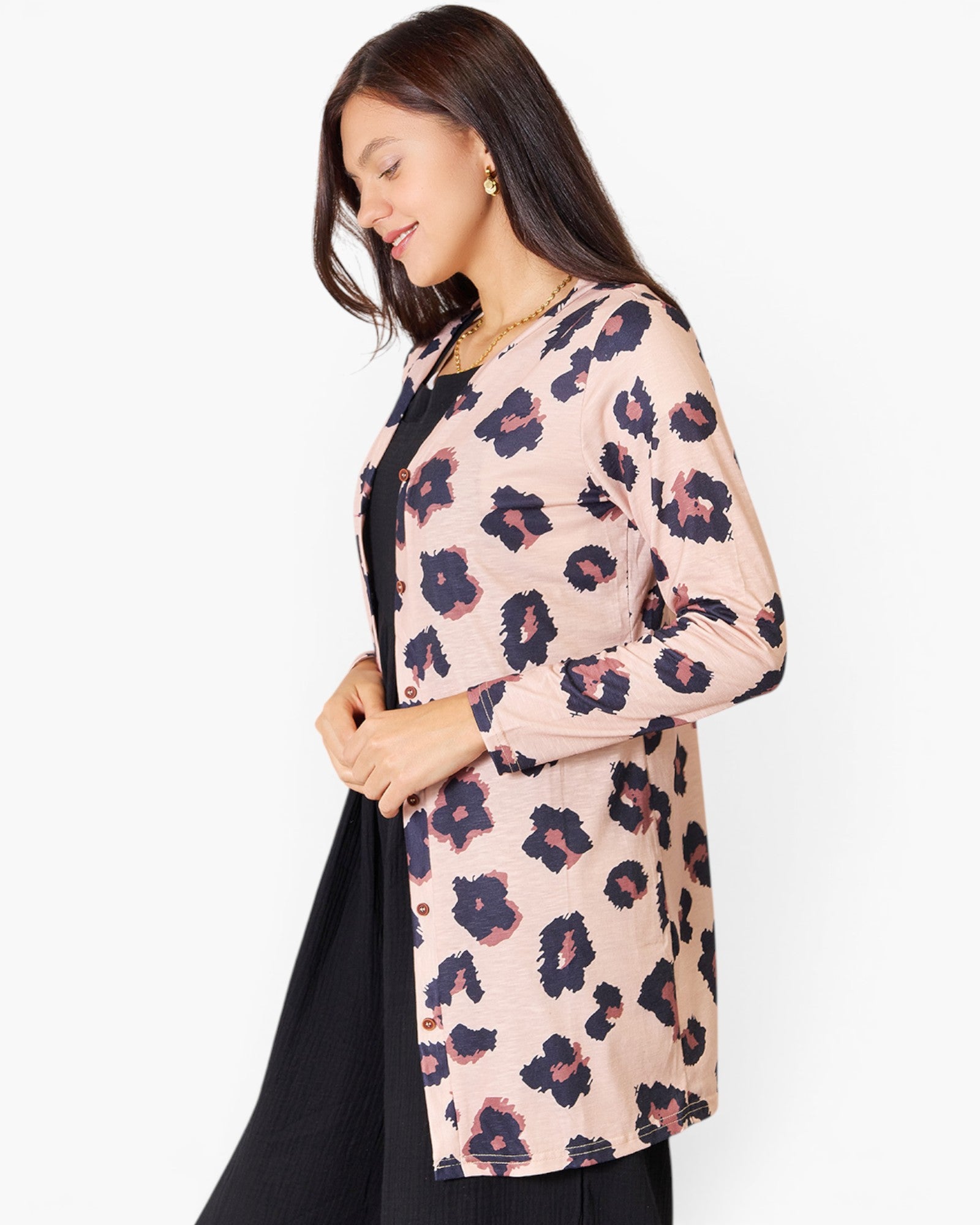 A woman wearing a light pink long-sleeve button-up cardigan with a dark navy and dusty rose floral print, layered over a black dress, against a plain white background.