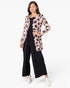 A woman modeling a light pink leopard-print cardigan over a black jumpsuit, paired with white sneakers, against a plain white studio background.