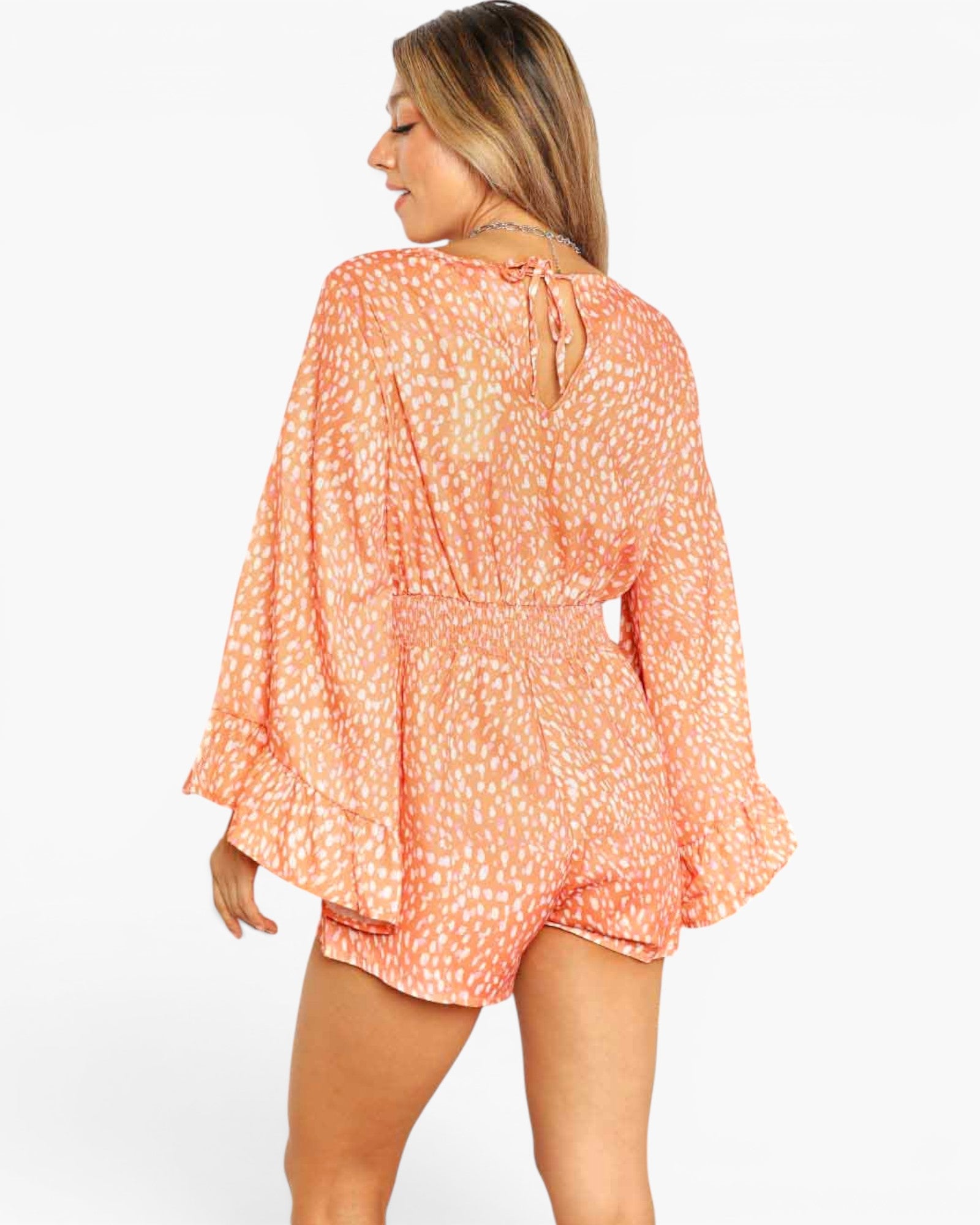 A woman shown from the back wearing a peach and white patterned romper with long bell sleeves and a tie detail at the neckline, against a plain light background.