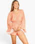 A woman modeling a peach and white patterned romper with long bell sleeves and a smocked waist, set against a plain light gray studio background.