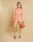 Woman wearing a coral floral romper against a beige paneled wall.