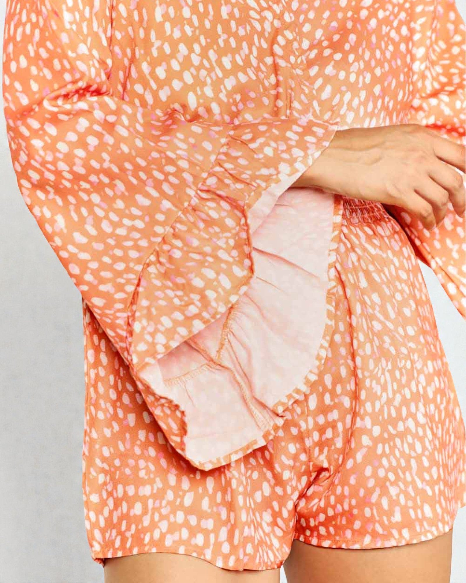 Coral patterned outfit with ruffled sleeves on a gray background