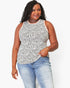 A woman modeling a sleeveless white top with a black irregular spotted pattern, paired with light blue jeans, against a plain white background.