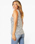 A woman wearing a sleeveless black and white spotted pattern top and light blue jeans, photographed against a plain white studio background.