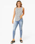 A woman modeling a sleeveless black and white patterned top with light blue skinny jeans and black wedge sandals, standing against a light gray studio background.