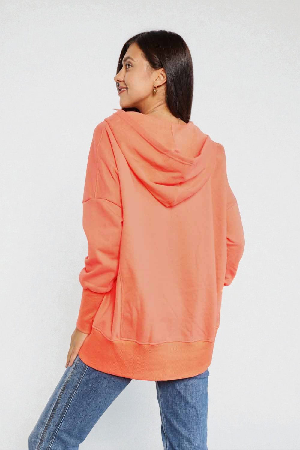Woman wearing a coral hoodie and blue jeans on a white background