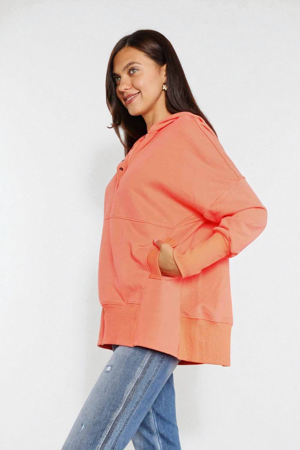 Woman wearing a coral hoodie and blue jeans on a white background