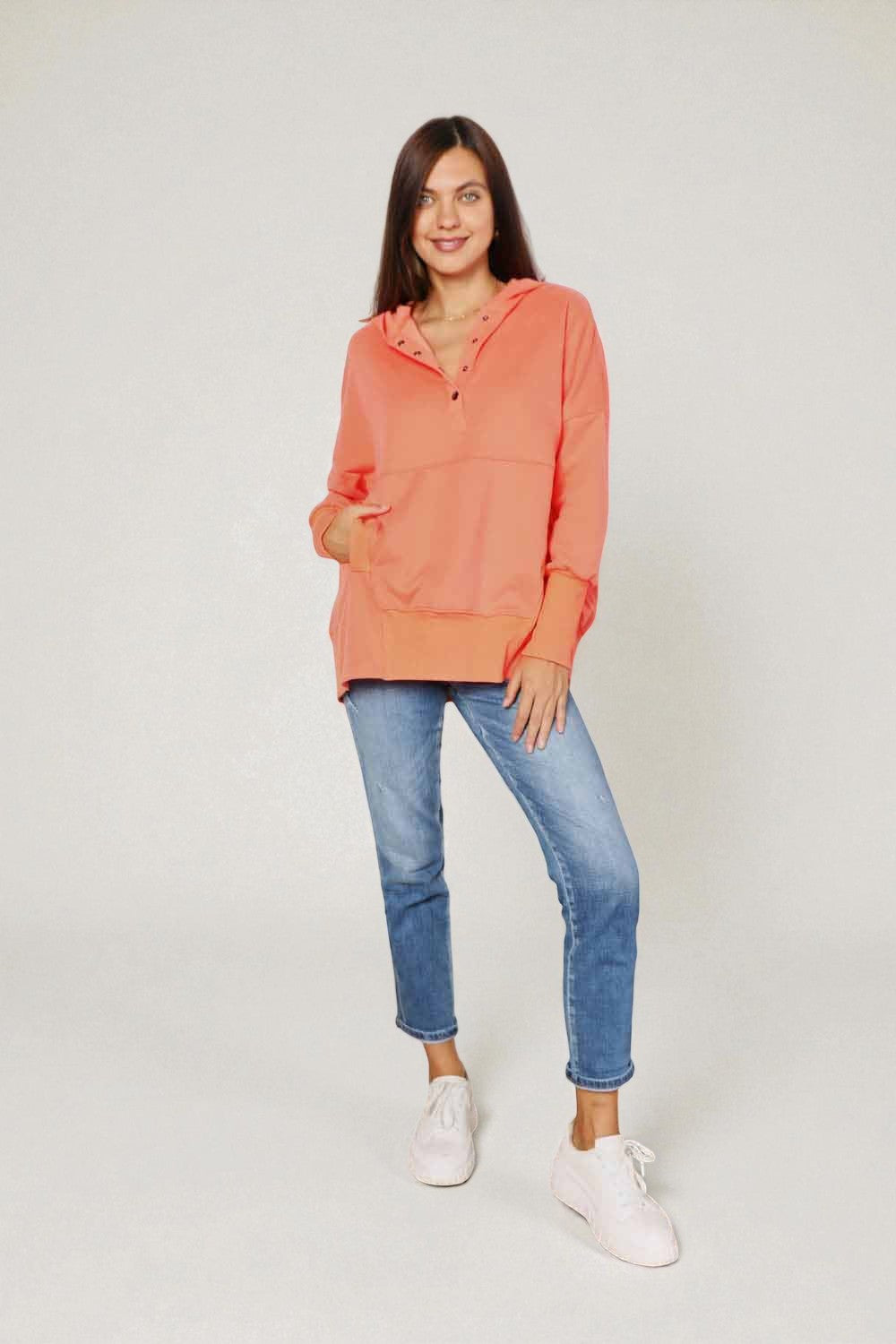 Woman wearing a coral hoodie and blue jeans on a white background
