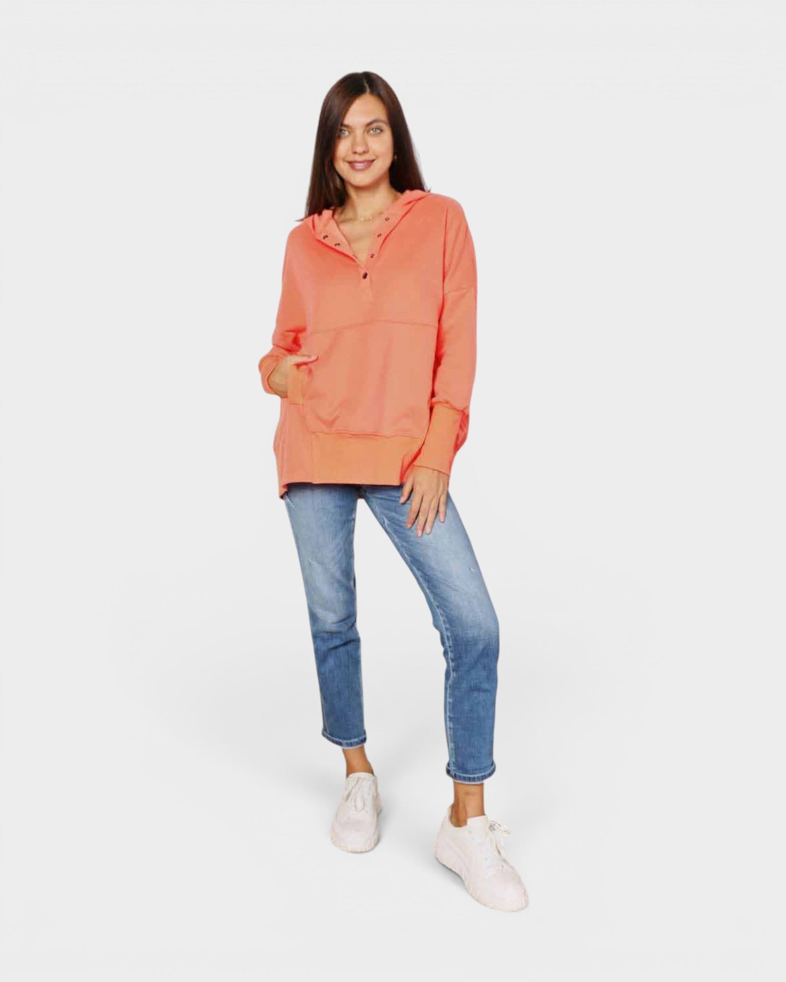 Woman wearing a coral hoodie and blue jeans on a white background