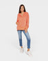Woman wearing a coral hoodie and blue jeans on a white background