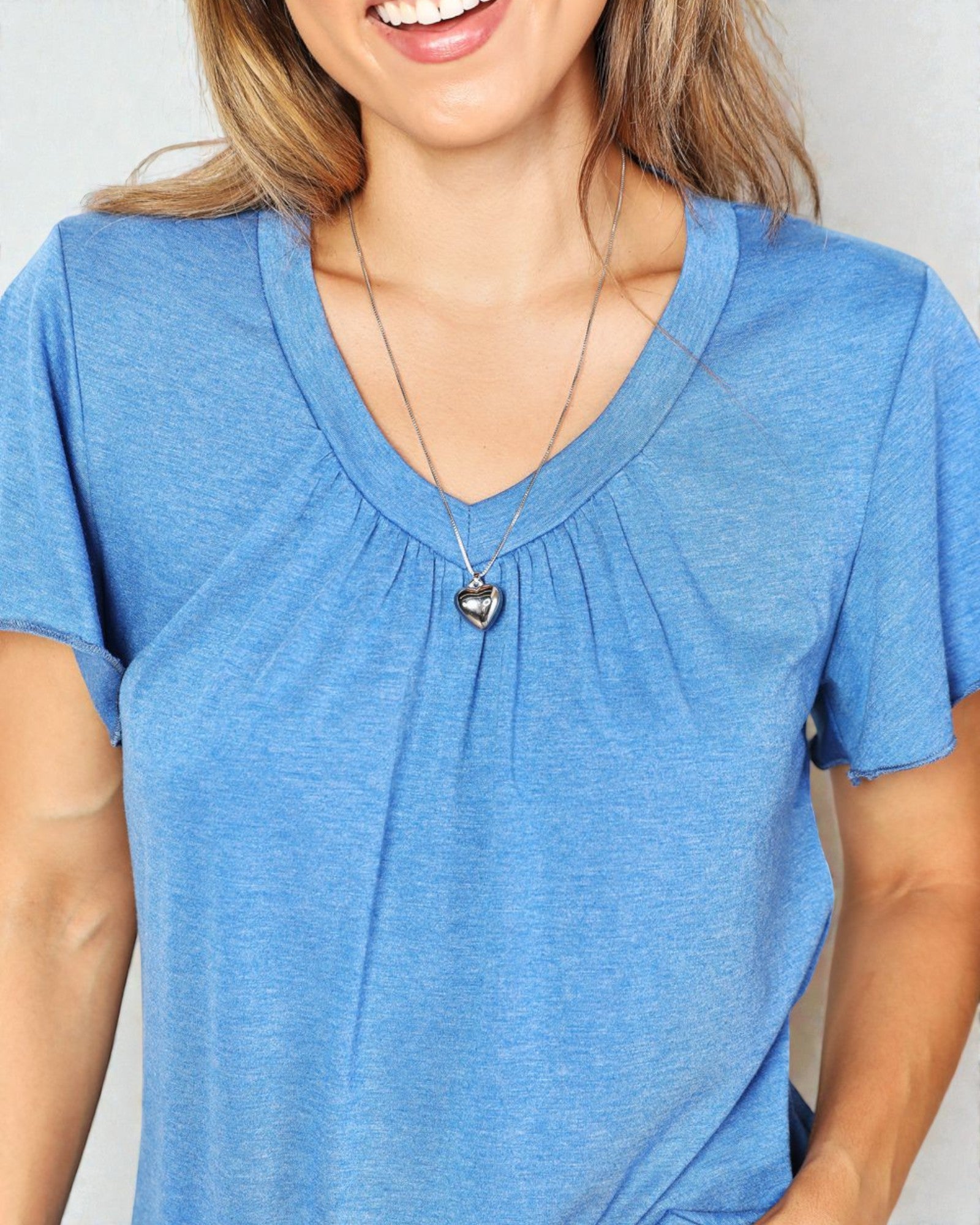 Woman wearing a blue shirt with a heart-shaped pendant necklace on a plain background