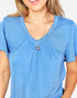 A woman wearing a heathered blue short-sleeve V-neck top with a gathered neckline and a silver heart pendant necklace, shown against a plain light background.
