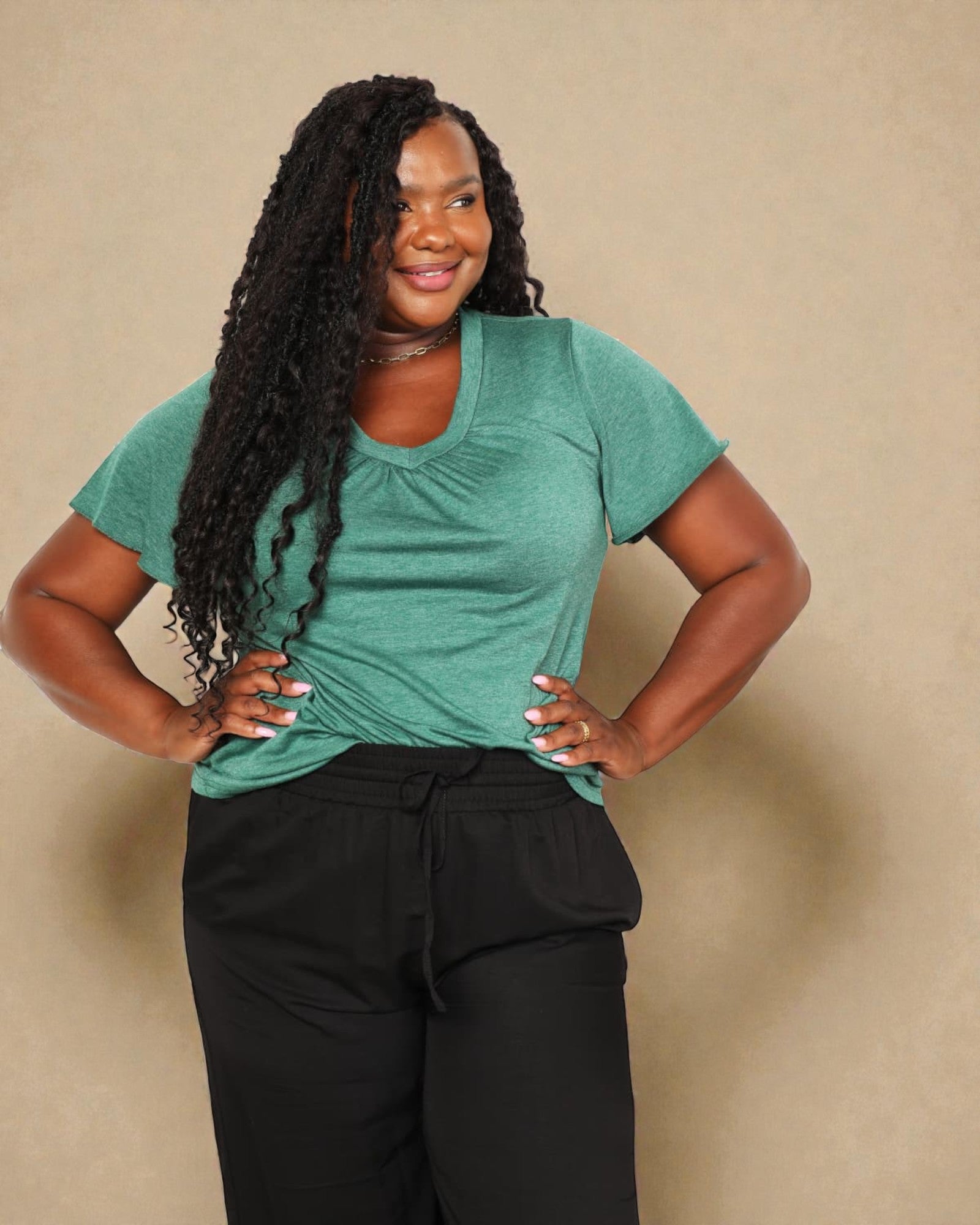 Woman wearing a teal shirt and black pants against a beige background