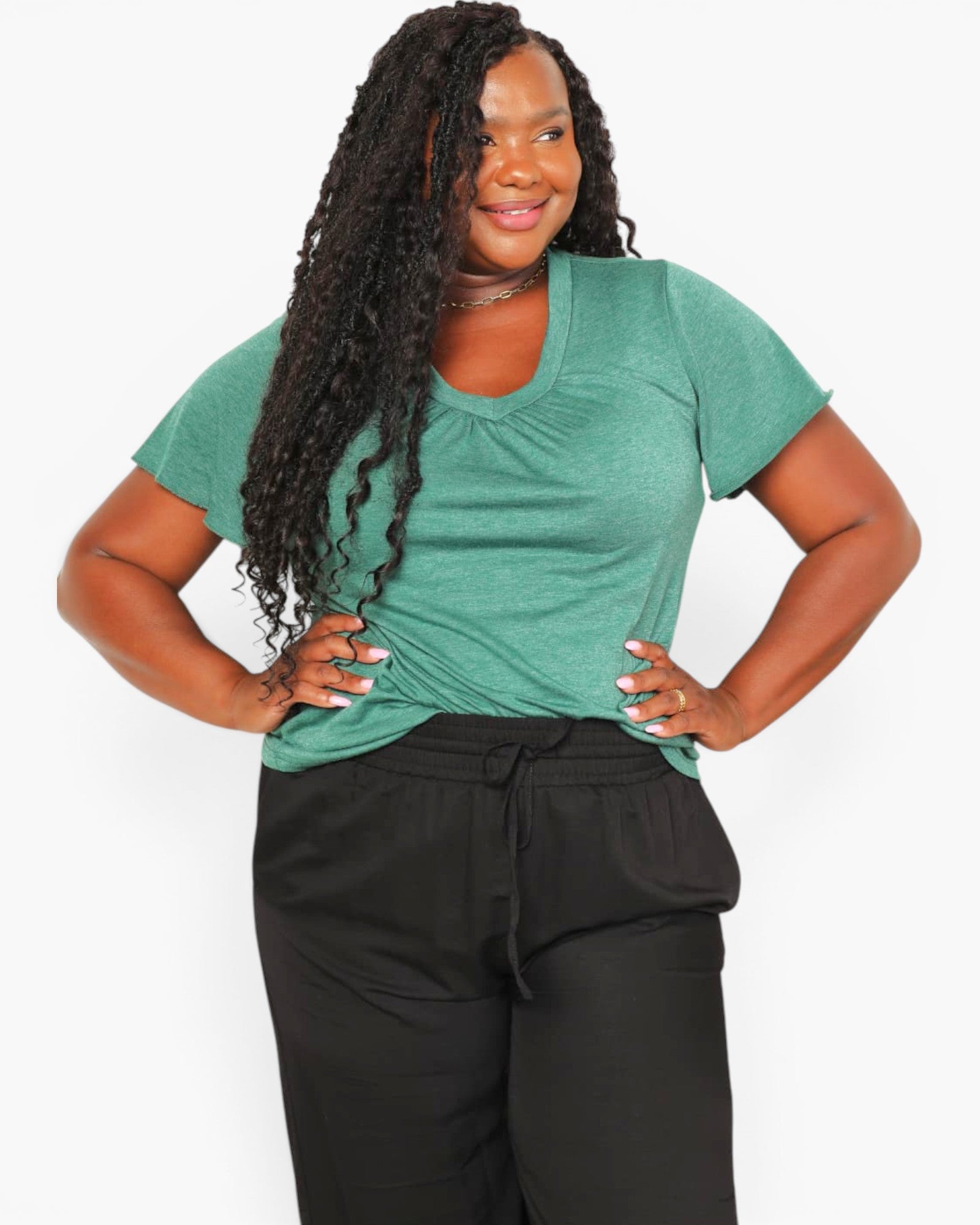 A woman modeling a short-sleeve green V-neck athletic top paired with black drawstring sweatpants against a light gray studio background.