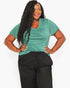 A woman modeling a short-sleeve green V-neck athletic top paired with black drawstring sweatpants against a light gray studio background.