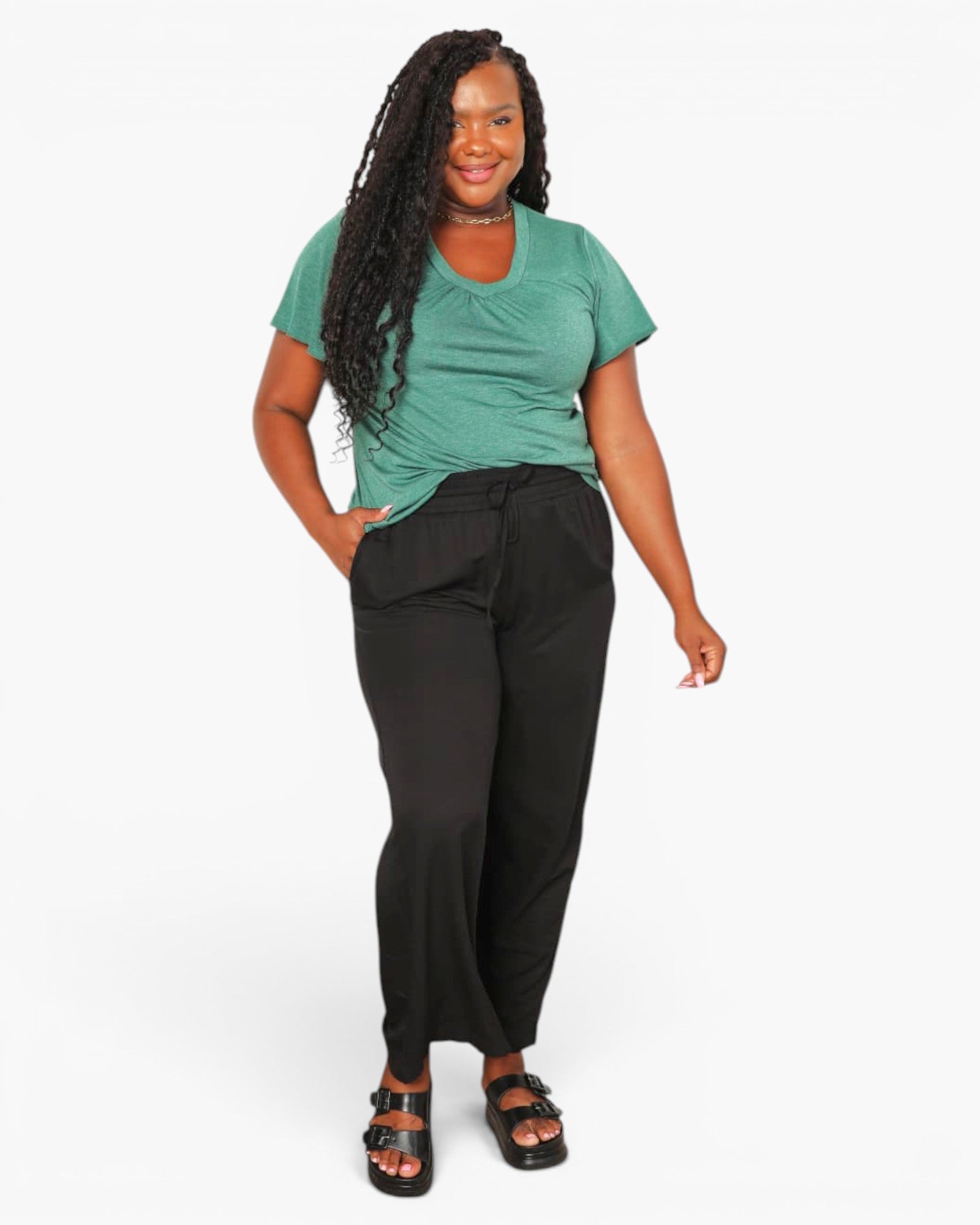 A woman modeling a short-sleeve green t-shirt and black wide-leg pants against a plain white studio background.