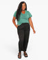 A woman modeling a short-sleeve green t-shirt and black wide-leg pants against a plain white studio background.
