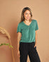 Woman wearing a green top and black pants against a brown background