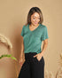 Woman wearing a green shirt and black pants against a beige background